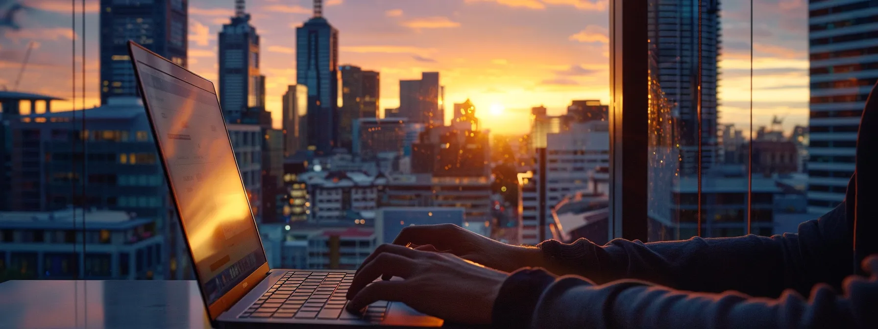 a person typing on a laptop with a view of the melbourne skyline in the background.